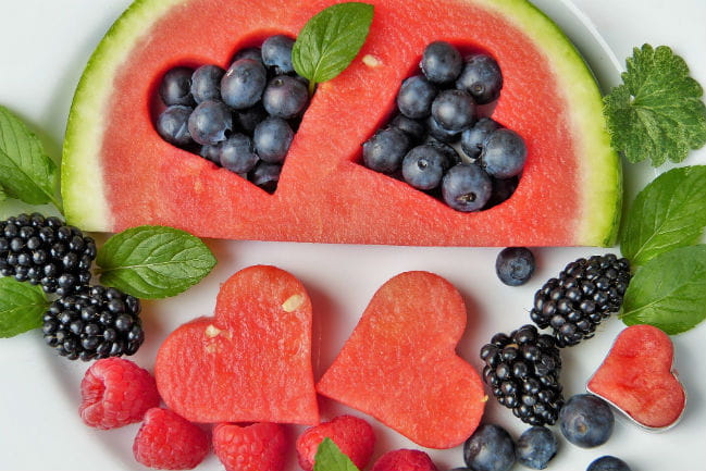Image of watermelon slice with heart shaped pieces cut out, blueberries, and blackberries.