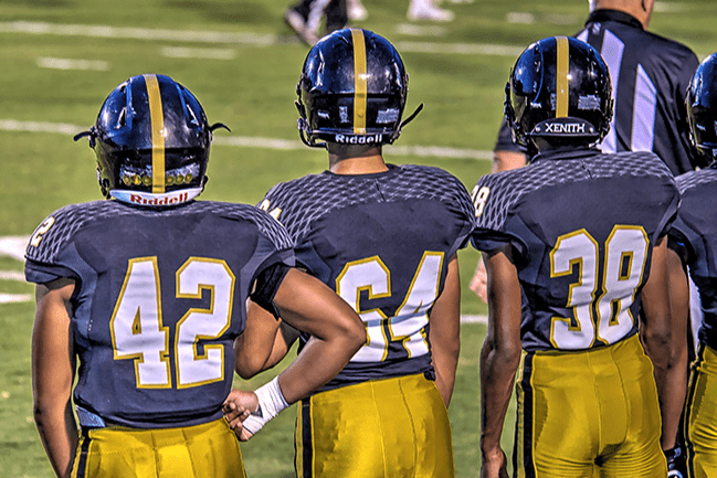 Three high school football players standing on the sidelines