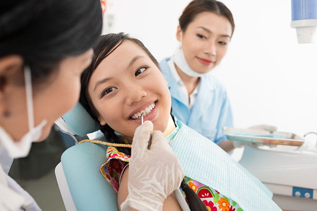 A dental hygienist examines a smiling patient's teeth. 