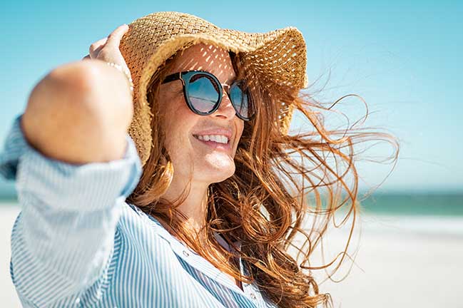 A smiling woman wearing a hat and sunglasses in Summer time at the beach