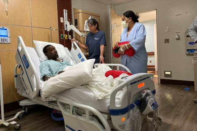 An MUSC patient in a hospital bed speaking with care team members.