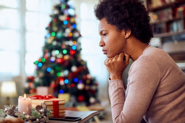 A young woman looks pensive as a Christmas tree stands in the background.