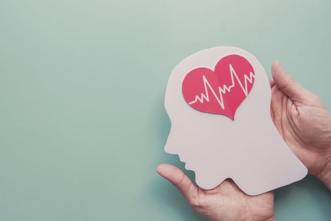 Decorative image of a pair of hands holding a cut-out drawing profile of a human head. Inside the head is the illustration of a heart with EKG lines on it. 
