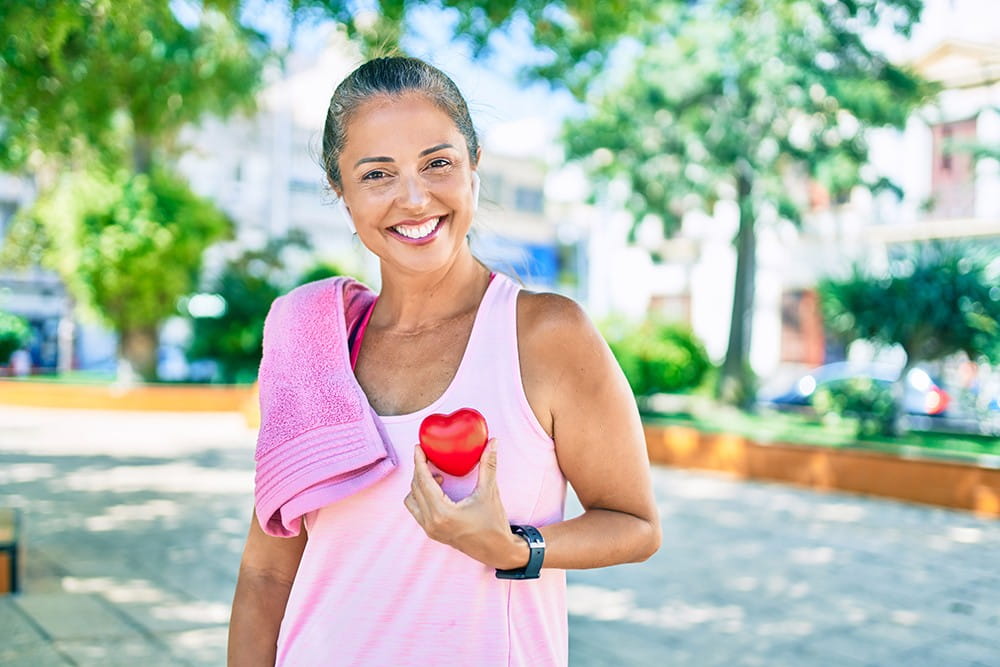 Middle age sportswoman asking for health care holding heart at the park.