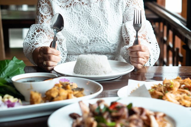 Person with plate of food in front of them holding a knife and fork.