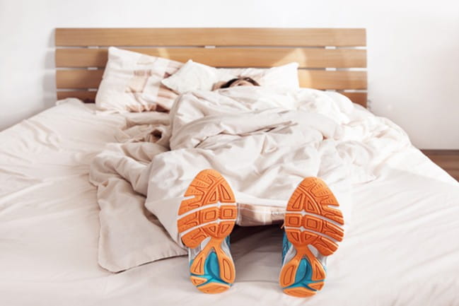A person in bed covered in a sheet except for their athletic shoes.