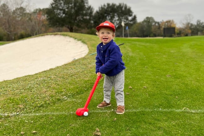 Smiling young child on a golf course with toy club.