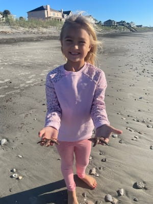 Smiling young girl on the beach holding starfish.