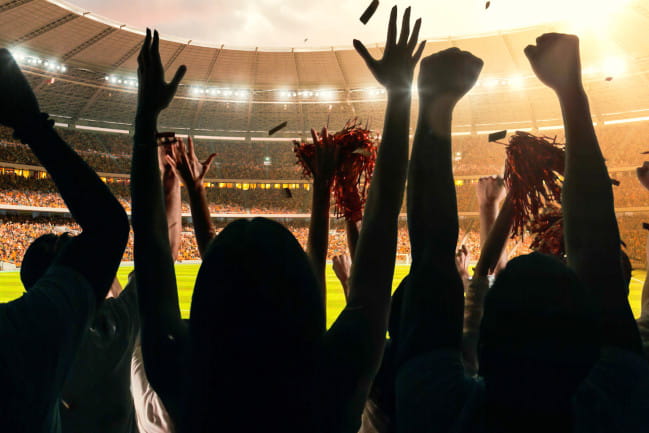 People in a stadium with their arms raised cheering.