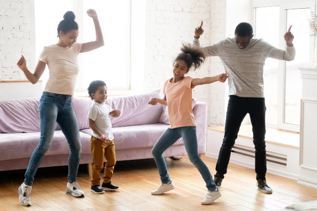 Two adults and two small children smiling and dancing indoors.