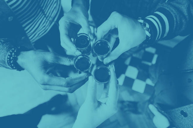 The hands of four people holding shot glasses together as a form of cheer.