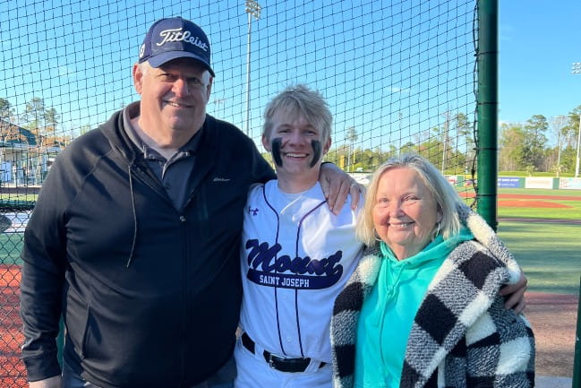 A Mike Bieda with two other smiling people outside at a baseball field.