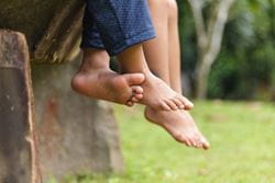 two pair of bare feet dangling from a bench