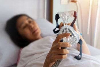 Patient in bed holding CPAP facemask