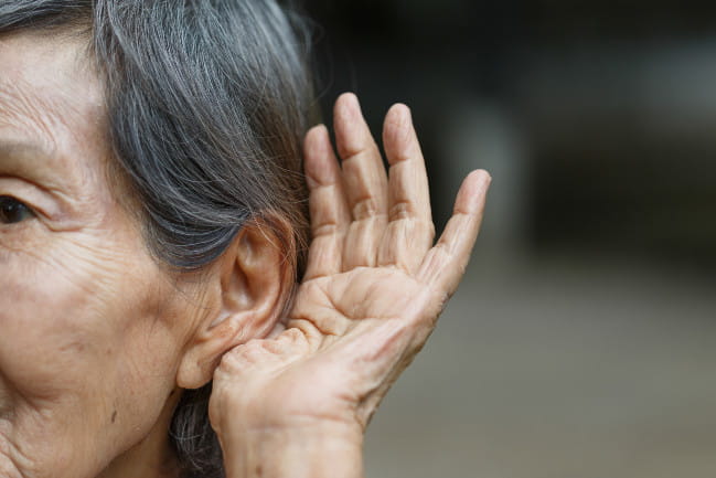Person cupping left hand to left ear in attempt to hear better.