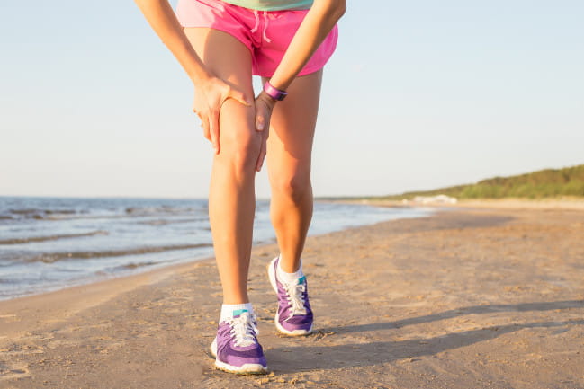 Person in athletic wear on a beach massaging their right quadracep.