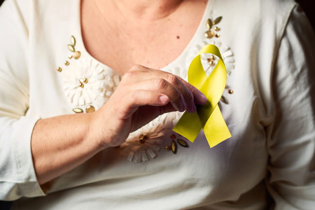 Person holding out yellow ribbon is affixed to their sweater. 