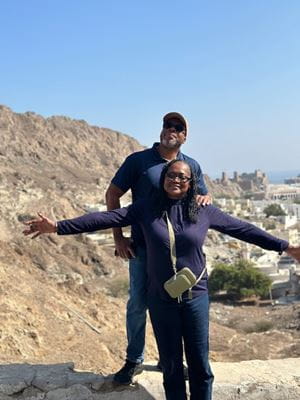 Smiling woman standing in front of smiling man. Her arms are stretched out to her sides. 