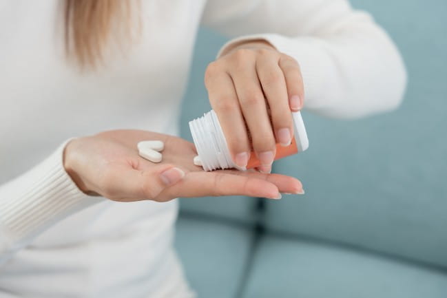 A person dispenses pills from a medicine bottle.