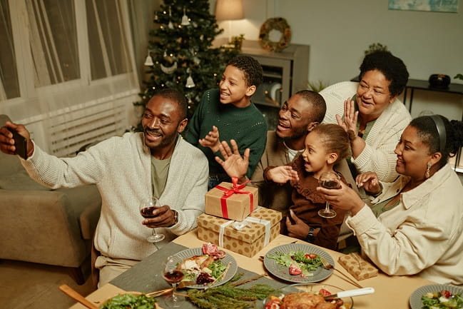 Smiling family at a table in front of a holiday tree taking a group photo.