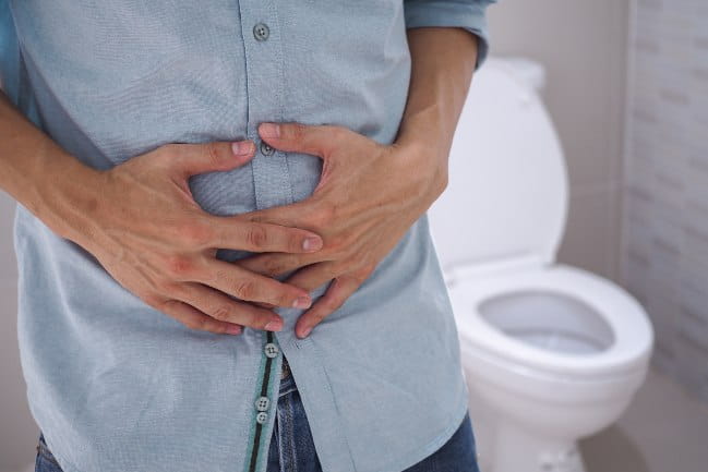 A person holding their stomach with a toilet in the background.