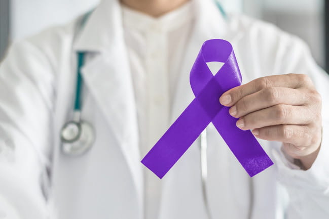 A doctor holding a purple ribbon to signify testicular cancer awareness.