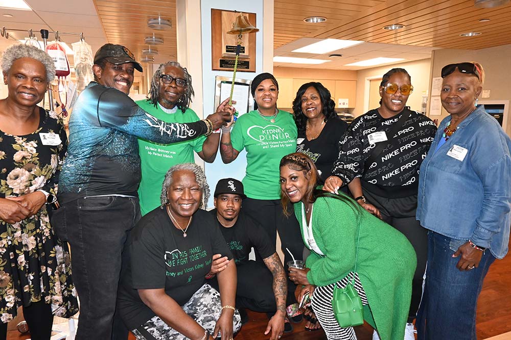 Group of happy looking people, some wearing green, gather to ring a bell.