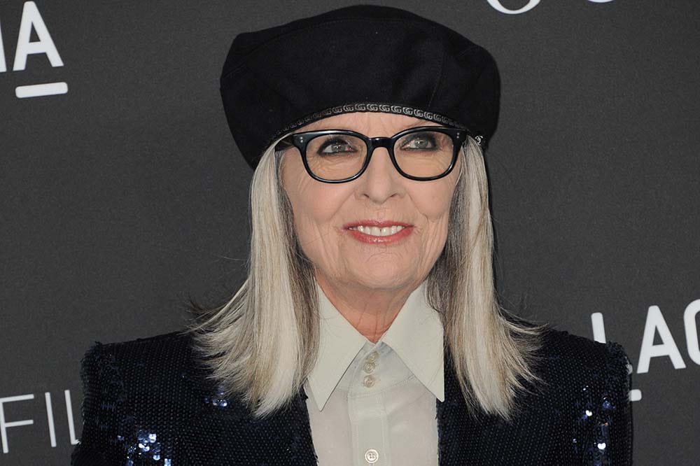 Woman with long silver hair wearing a black cap and black glasses.